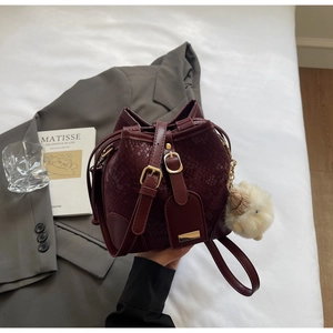 Detail of burgundy snakeskin bucket bag with plush charm on a chic aesthetic background