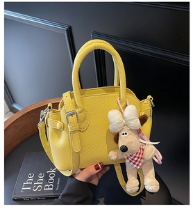 Detail of yellow lychee texture handbag featuring a cute dog plush charm on a wooden table