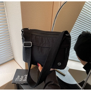 Close-up of black nylon crossbody bag with multi-zipper layers and metallic logo