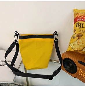 Dettaglio di una borsa a tracolla in nylon giallo con cinturino nero e bottone a pressione