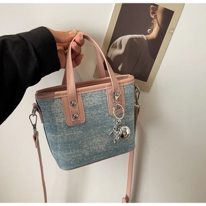 Detail of blue denim bucket bag with pink leather trim and shiny balloon dog charm
