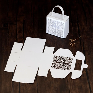 Detail of white laser-cut paper gift box with cross pattern on dark wood background