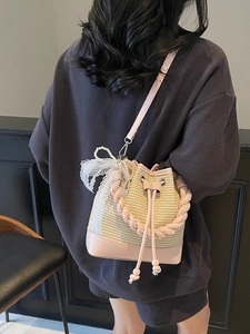 Pink woven bucket bag with pearl charm and lace bow shown on a model side view