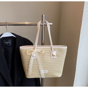 Détail d'un sac en paille tissée avec un nœud en dentelle blanche et des anses fines