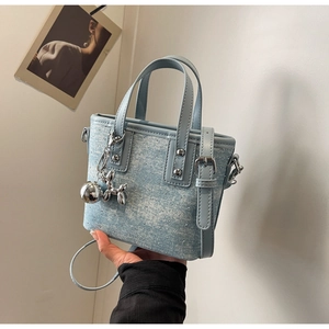 Detail of light blue denim mini tote with crystal studs and a silver dog charm accessory