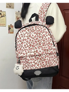 Detail of pink leopard print backpack with plush mascot charm and black fabric trim