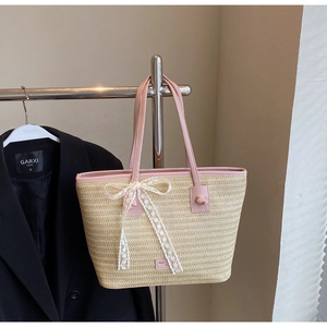 Détail d'un sac cabas en paille tissé avec anses en cuir rose et noeud en dentelle
