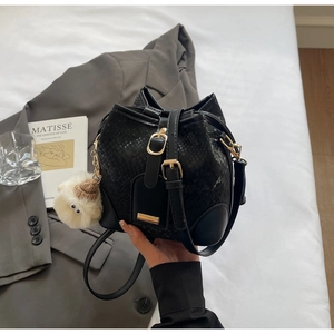 Detail of black faux-snakeskin bucket bag with gold hardware and white plush charm