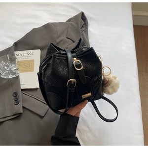 Detail of black snake-embossed bucket bag with gold hardware and white plush charm
