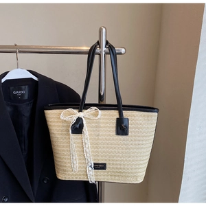 Détail du sac cabas en paille tissé avec bordure en cuir noir et nœud en dentelle blanche