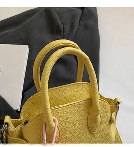 Detail of yellow litchi grain leather handbag handle with pink side hooks and metal buckle