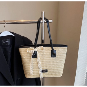 Détail d'un sac cabas en paille tissée avec anses en cuir noir et nœud en dentelle