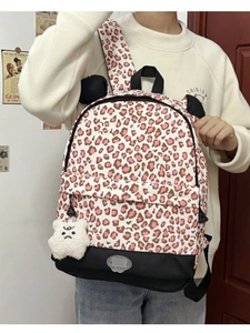Leopard print backpack with plush bear pendant shown on model in casual indoor setting