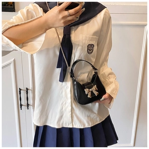 Détail d'un mini sac à bandoulière en cuir noir avec boucle nœud doré et chaîne métallique