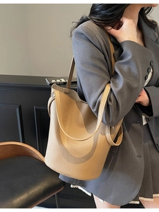 Beige lychee leather bucket bag with wide handles and metal lock worn by a female model