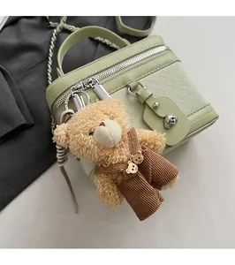 Détail du sac boîte tissé vert clair avec fermeture argentée et charme d'ours en peluche