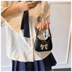 Vue détaillée du mini sac à main noir avec un grand nœud doré porté par un modèle