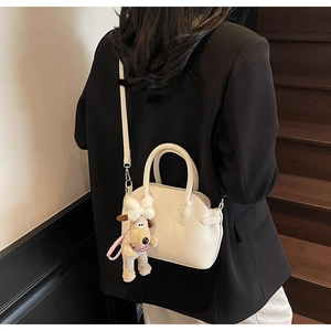 Chic cream shell bag in lychee pattern worn crossbody with cute puppy charm accessory