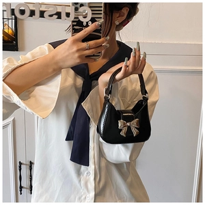 Détail du sac croissant en cuir verni noir avec boucle nœud argenté sur chemise blanche