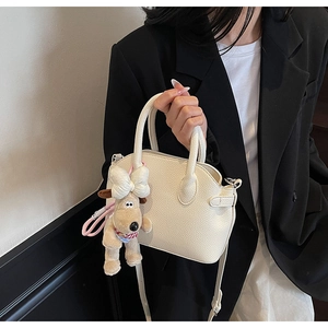 Primer plano del bolso de concha beige con grano de lichi y colgante de perro de peluche