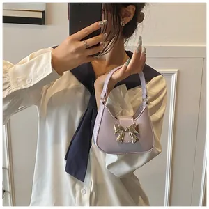 Détail d'un mini sac à main lilas avec un fermoir nœud doré et bandoulière chaîne