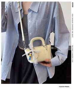 Detail of cream leather shoulder bag with lace bow, pearl charm, and doll pendant