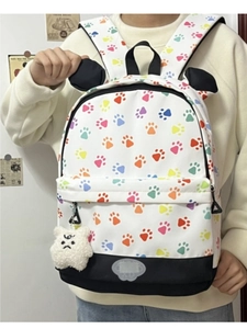 Detail view of white backpack with colorful paw prints and plush charm on a model