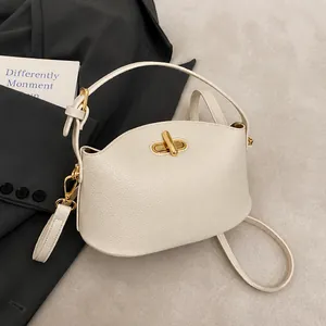 Detail der cremeweißen Handtasche mit Litschi-Struktur und goldenem Drehverschluss