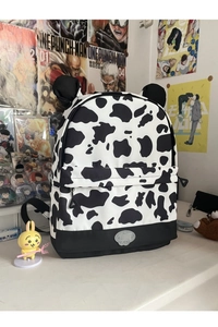 Detail of a cow print backpack featuring cute decorative ears and a front zipper pocket