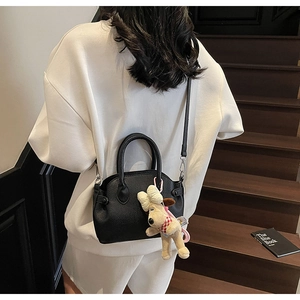 Bolso de cuero granulado negro con colgante de perro de peluche en una escalera de madera