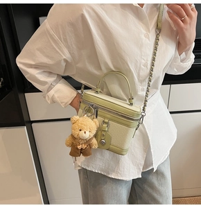 Détail du sac boîte vert clair avec texture tissée, finitions argentées et breloque ours