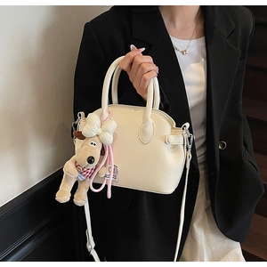 Detalle de bolso concha de cuero blanco crema con un lindo colgante de perro de peluche