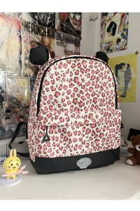 Detail of leopard print backpack with decorative 3D ears and circular metal logo plaque