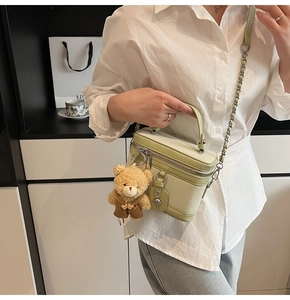 Détail du sac boîte vert clair tressé avec breloque ours en peluche amovible et bandoulière