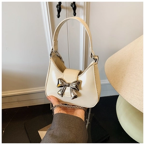 Détail d'un mini sac à main beige avec un grand nœud argenté et une bandoulière chaîne