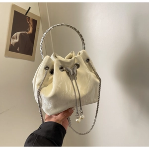 Gros plan d'un sac seau crème avec breloque papillon argentée et détails en perles