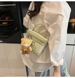 Détail du sac boîte vert clair avec texture tissée, chaîne en métal et breloque ourson