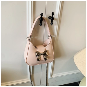 Détail du mini sac rose clair avec nœud doré suspendu à une porte blanche élégante
