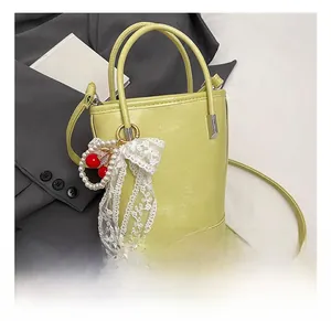 Détail du sac seau en cuir vert clair avec breloques cerise et perles décoratives