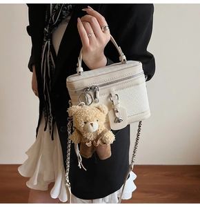 Détail d'un sac à main tressé crème avec breloque ours en peluche et chaîne argent