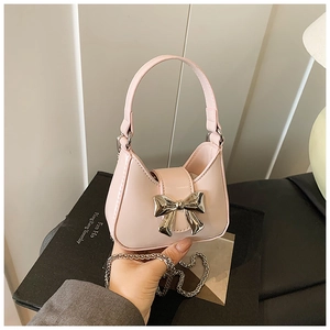 Mini sac à main rose avec nœud argenté et bandoulière chaîne, tenu à la main en vue