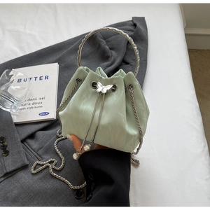 Détail du sac seau vert clair avec fermoir papillon et pompon en perles sur le cordon