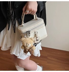 Détail du sac bowling tissé crème avec pendentif ours porté par un mannequin