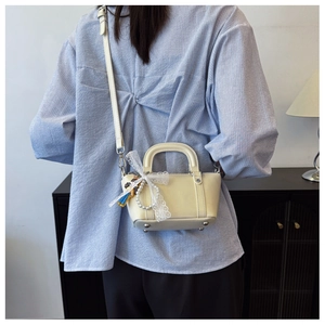 Detail of cream crossbody bag featuring pearl chain, lace bow, and protective bottom rivets