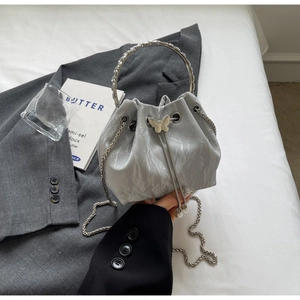 Détail du sac seau argenté avec boucle papillon en métal et poignée anneau cristal
