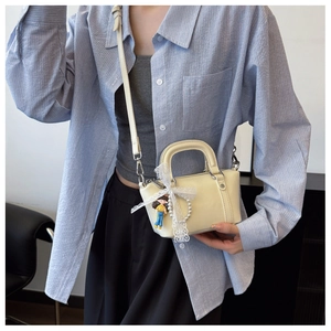 Detail of off-white mini handbag featuring lace bow, pearl charm, and doll pendant