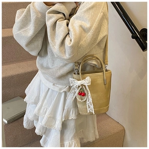 Détail du sac seau beige élégant orné d'un nœud en dentelle et d'un pendentif cerise et perle