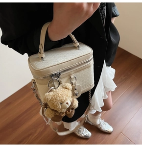 Détail du sac seau tressé crème avec pendentif ours et bandoulière chaîne sur modèle