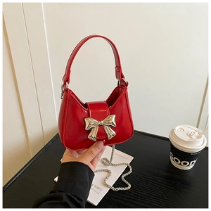 Détail d'un mini sac en cuir verni rouge avec nœud argenté et bandoulière en chaîne