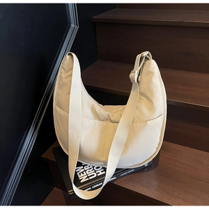 Detail einer großen beigen Nylon-Halbmondtasche mit verstellbarem Gurt auf einem Buch und Treppe